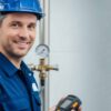 Smiling caucasian man in blue uniform and hardhat holding detector. Gas specialist inspecting city gas system. Industrial worker.